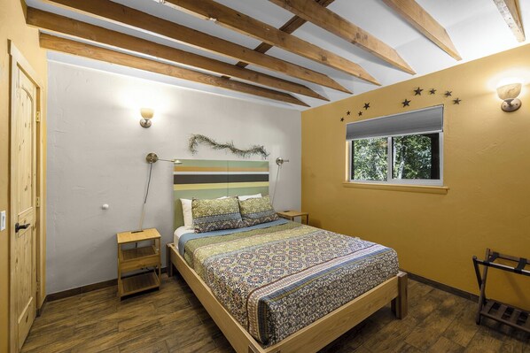 Een slaapkamer met een houten bed, nachtkastje, raam en een wandlamp.