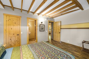 Une chambre à coucher avec un grand lit, des portes en bois et un plafond en pente avec des poutres apparentes.