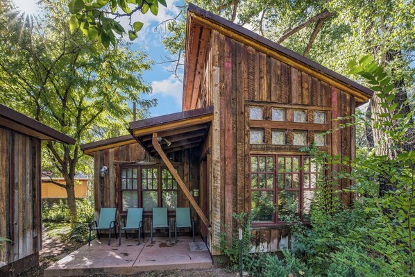 A rustic wooden cabin with a covered patio area, large windows, and a view of the surrounding forest.
