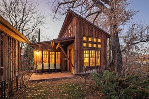 A rustic wooden cabin with a porch, large windows, and a small table and chair set outside.