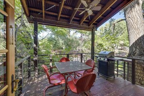 An outdoor patio with a table and chairs, a grill, and a view of the surrounding trees.