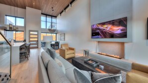 Amplia sala de estar con un televisor de pantalla plana grande, una chimenea y una cocina moderna al fondo.
