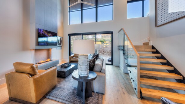 Un salón amplio con chimenea, un sofá, una mesa de centro y una escalera con barandilla de cristal.