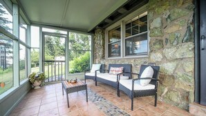 A covered patio with wicker furniture, stone walls, and a view of the outdoors. - Unwind in a charming historic cottage near Nelson 151 featuring a Level 2 EV outlet, modern comforts, and easy access to Virginia's wineries, breweries, hiking trails, and Blue Ridge scenery. (Afton)