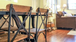 A dining area with wooden chairs and a table, a sofa, and a lamp in the background. - Unwind in a charming historic cottage near Nelson 151 featuring a Level 2 EV outlet, modern comforts, and easy access to Virginia's wineries, breweries, hiking trails, and Blue Ridge scenery. (Afton)