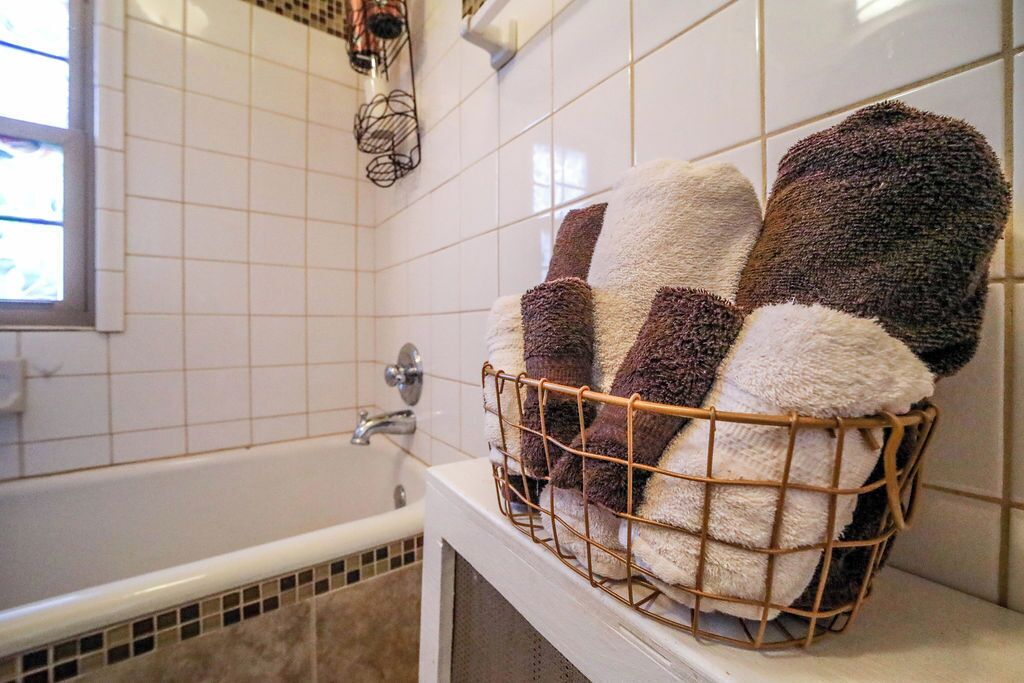 A bathroom with a white bathtub, a towel rack with a wire basket holding several towels, and a window with a view of the outside.