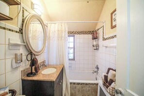 Une salle de bain avec un meuble-lavabo à deux vasques, un grand miroir, une douche avec un rideau et une petite fenêtre.