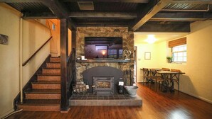 A staircase leading to a stone fireplace with a television above it, a dining area with wooden furniture, and a window with blinds. - Unwind in a charming historic cottage near Nelson 151 featuring a Level 2 EV outlet, modern comforts, and easy access to Virginia's wineries, breweries, hiking trails, and Blue Ridge scenery. (Afton)