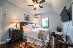 Une chambre à coucher comprenant un lit, deux lampes de chevet, un ventilateur de plafond, un téléviseur fixé au mur et une fenêtre.