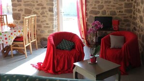 A cozy room with a stone wall, a dining table with a polka dot tablecloth, two red chairs, a small table with a plant, and a television on a stand. - Charming stone cottage near Guérande (Guérande)