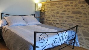 A bed with a metal frame and white bedding in a room with stone walls and a wooden floor. - Charming stone cottage near Guérande (Guérande)