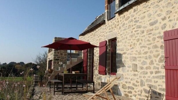 A stone building with a red umbrella and outdoor seating. - Charming stone cottage near Guérande (Guérande)