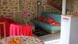 A cozy room with a stone wall, a teal sofa with red cushions, a small table with a polka dot tablecloth, and a bowl of oranges. - Charming stone cottage near Guérande (Guérande)