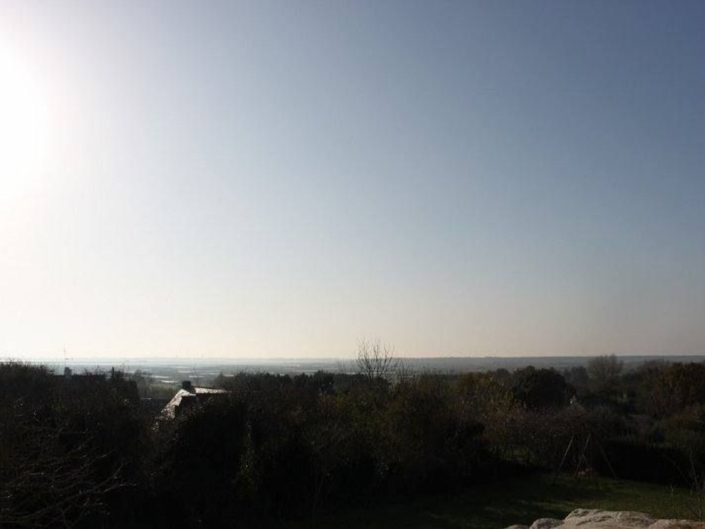 Un paysage rural avec un ciel dégagé, une maison visible au loin et une végétation luxuriante au premier plan.