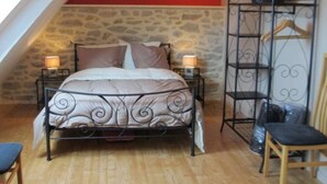 A bedroom with a stone wall, a bed with a metal frame, two bedside lamps, a wooden chair, and a metal shelf unit.