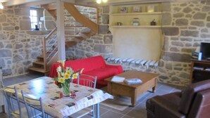 A cozy living room with a stone wall, a red sofa, a dining table with metal chairs, and a staircase.