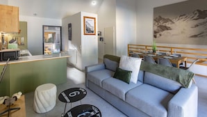 A modern living room with a grey sofa, a small round table, and a dining area with a mountain view mural.