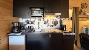 Une cuisine compacte dotée de meubles de rangement sombres, d’un four à micro-ondes, d’une machine à café et d’un petit réfrigérateur.