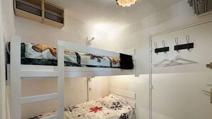 Une chambre avec un lit superposé, un mur blanc, une porte avec un porte-manteau et un luminaire.