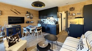 Un salon moderne comprenant un canapé, une table à manger avec des chaises, un coin cuisine avec des placards et des appareils électroménagers, et un téléviseur fixé au mur.