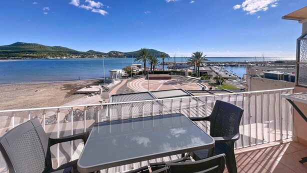 A balcony with a glass table and chairs overlooking a beach and marina.