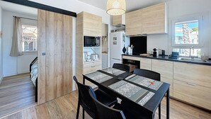 A modern kitchen with wooden cabinets, a dining table with black chairs, and a hanging light fixture.
