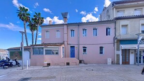 A pink building with a tiled roof, a blue door, and a small entrance. There are palm trees and a scooter parked outside.
