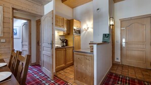 A cozy kitchen with wooden cabinets and a tiled floor, a dining area with a plaid tablecloth, and a wooden door.