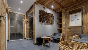 A modern interior with a wooden ceiling, a wall-mounted mirror art piece, a wicker chair, and a small table.