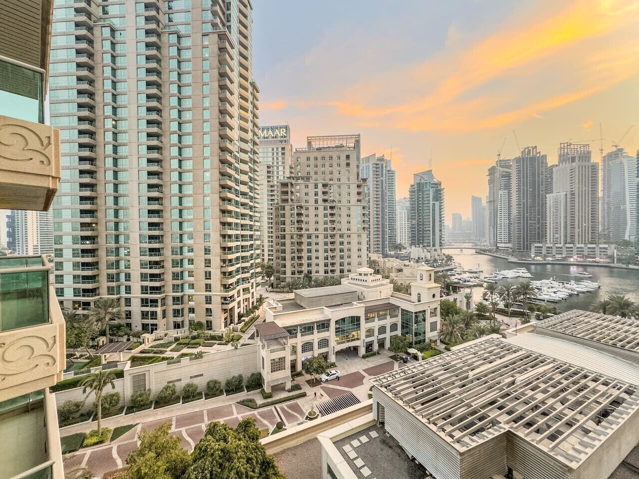 A high-rise residential building with multiple balconies, a marina with boats, and a river in the background.
