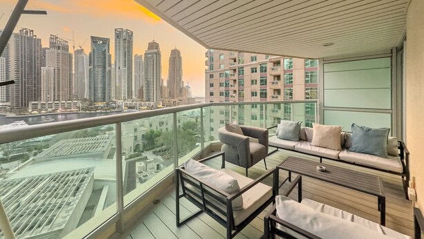 A balcony with a city view, furnished with a sofa, chairs, and a table.