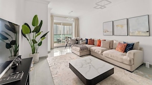 A modern living room with a beige sofa, a coffee table, and a large window with a view of high-rise buildings.