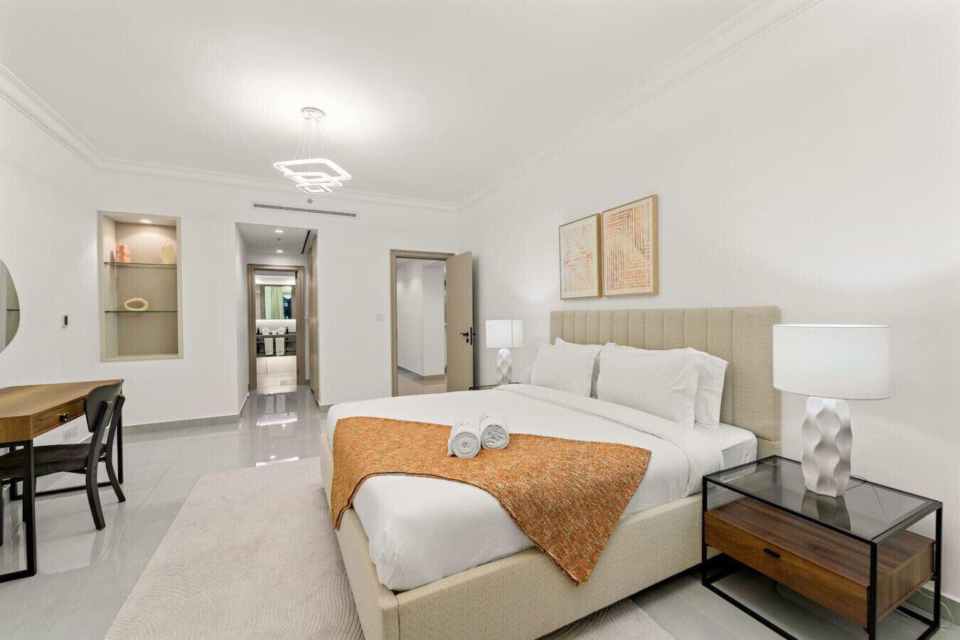 A modern hotel room with a large bed, bedside tables, a desk, and a bathroom visible through an open door.
