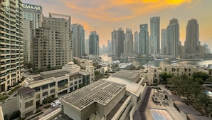 A high-rise building with a prominent EMAAR sign, surrounded by other tall buildings and a body of water in the background.