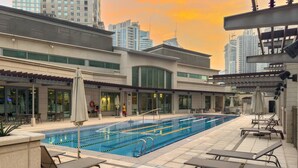 An indoor swimming pool with clear lane dividers, sun loungers, and a view of the cityscape in the background.