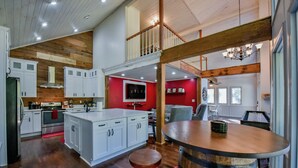 A spacious kitchen with white cabinets, a central island, and a red accent wall. - Legends Lodge: A woodland retreat near University of Alabama! (Cottondale)