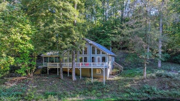 A house with a deck and a dock extending into a clear pond surrounded by trees. - Legends Lodge: A woodland retreat near University of Alabama! (Cottondale)