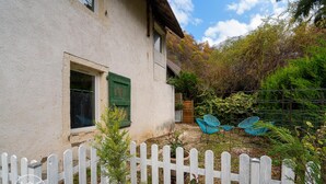 A white house with a wooden fence, a window with green shutters, and a garden with potted plants and blue chairs. - The refuge at the end of the world (saint alban leysse)