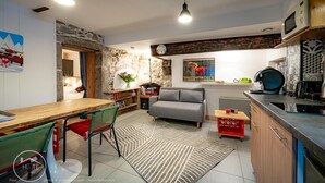 A modern kitchen with a dining area, stone wall, and a sofa. - The refuge at the end of the world (saint alban leysse)