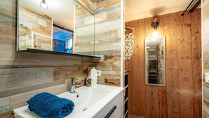 A bathroom with a wooden wall, a white sink, a blue towel, and a mirror. - The refuge at the end of the world (saint alban leysse)