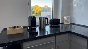 Une cuisine équipée d’une machine à café, d’une bouilloire, d’un grille-pain et d’une boîte en bois contenant divers objets colorés, le tout posé sur le plan de travail.