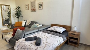 Une chambre à coucher moderne avec un canapé gris, une table de chevet en bois, une petite table et un grand miroir.