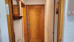A narrow hallway with a wooden door at the end, a radiator on the left, and a tiled floor. - 2 bedroom appt 20 mins from Morzine and rest of Portes du Soleil (Le Biot)