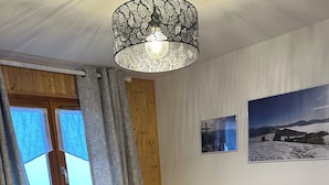 A bedroom with a bed, a radiator, a window with curtains, a wall-mounted picture, and a ceiling light fixture. - 2 bedroom appt 20 mins from Morzine and rest of Portes du Soleil (Le Biot)