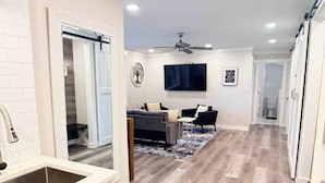 A modern kitchen with a large island, a dining area with a sofa and chairs, and a hallway leading to a bathroom.