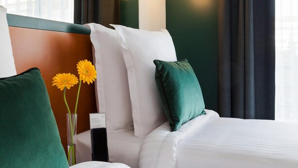 A hotel room with a bed, green and white pillows, a vase with flowers, and a sign on the nightstand. - Spacious Apartment to Accommodate up to 4 People (Cannes)