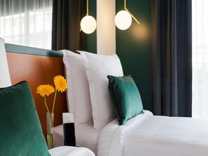 Ein Hotelzimmer mit Bett, grünen und weißen Kissen, einer Vase mit Blumen und einem Schild auf dem Nachttisch.