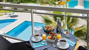 A balcony with a breakfast setup including coffee, juice, and fruit, overlooking a swimming pool and lush greenery. - Spacious Apartment to Accommodate up to 4 People (Cannes)