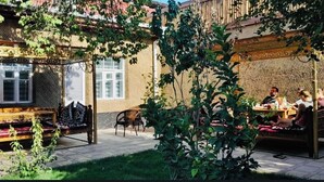 Un espacio al aire libre con un banco y una mesa de madera, rodeado de vegetación y un edificio con paredes decoradas.