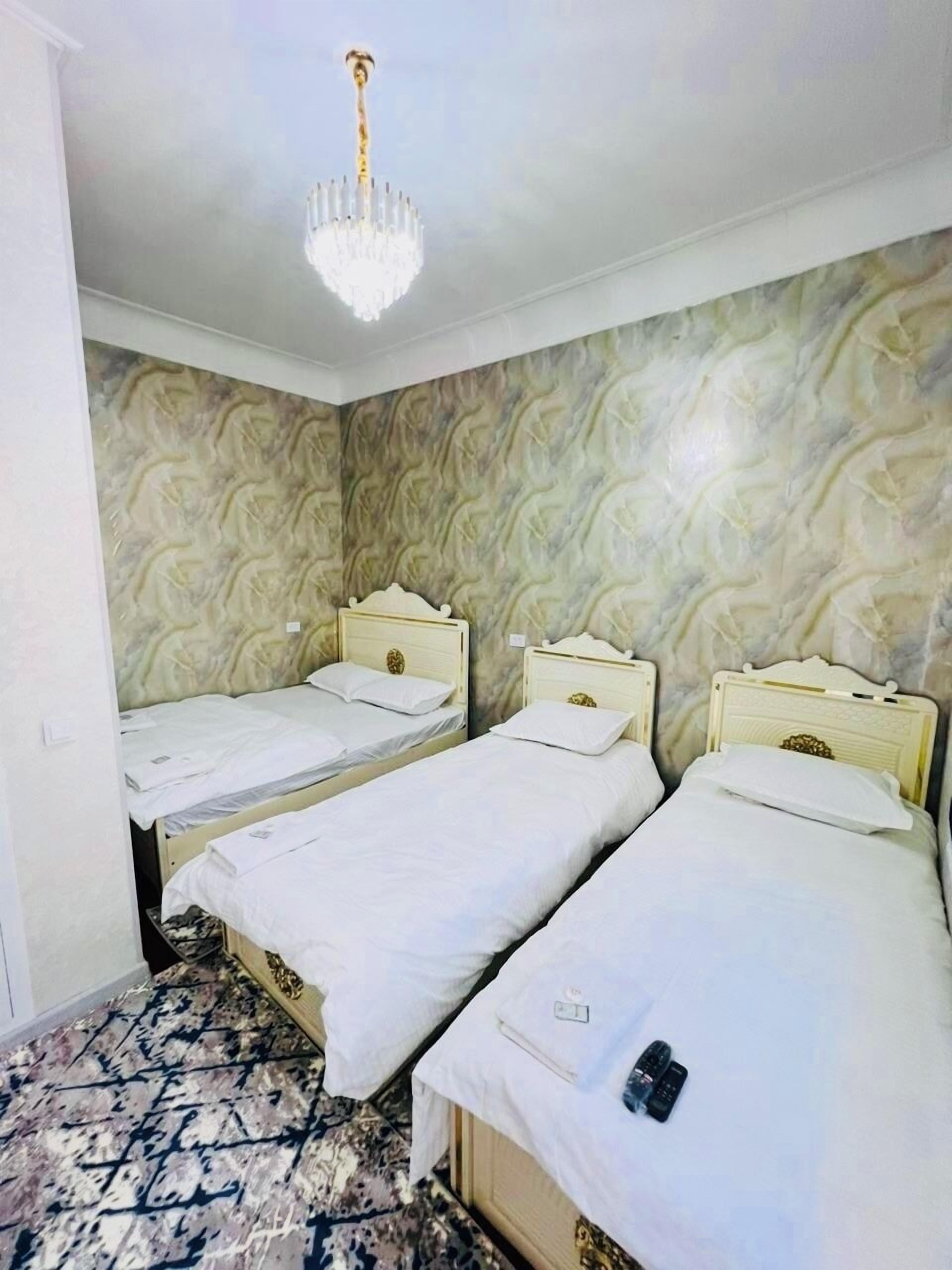 Une chambre d’hôtel avec trois lits simples, un lustre et un mur orné d’un motif.